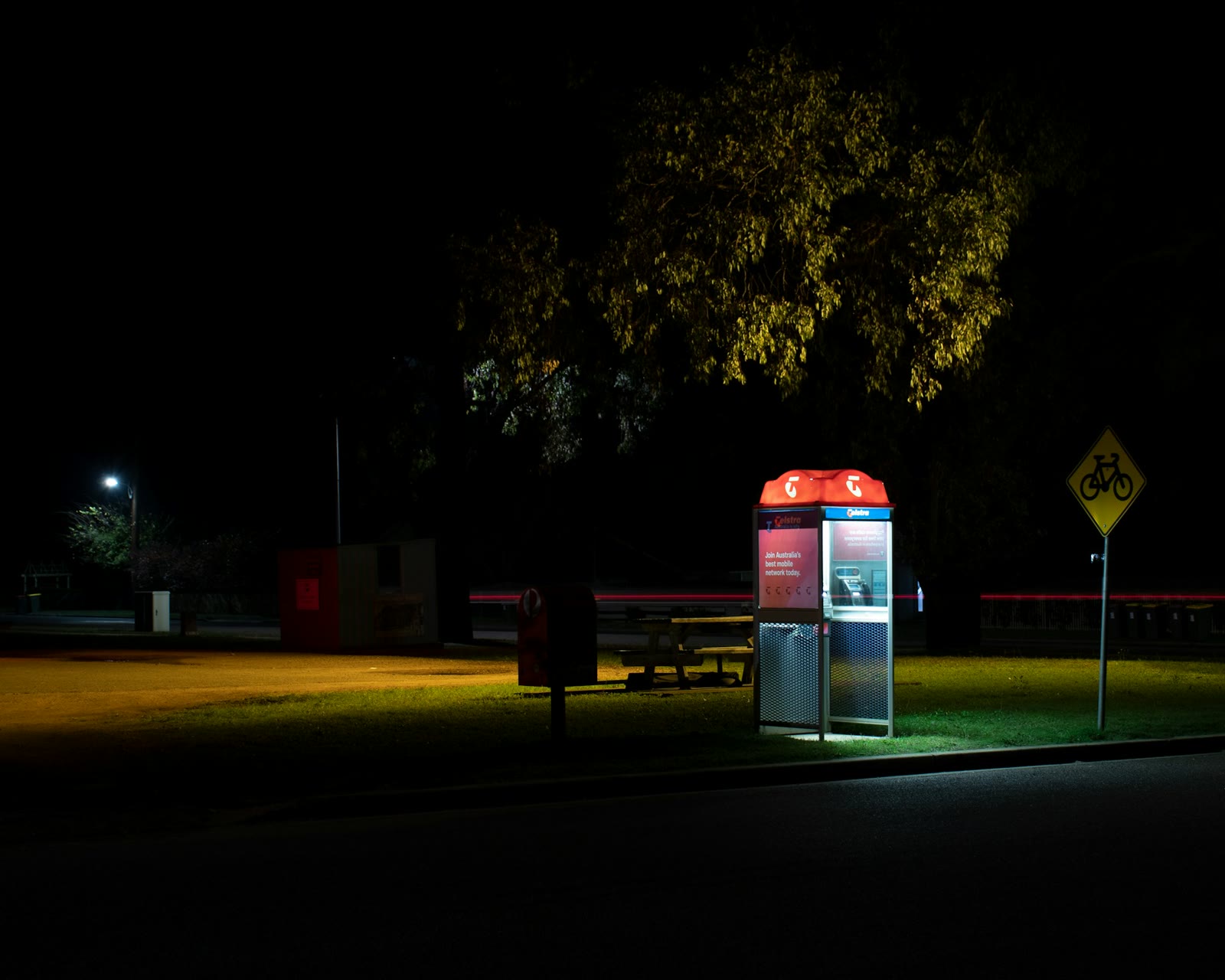 Telstra phone box lit up at night on an empty Australian roadside